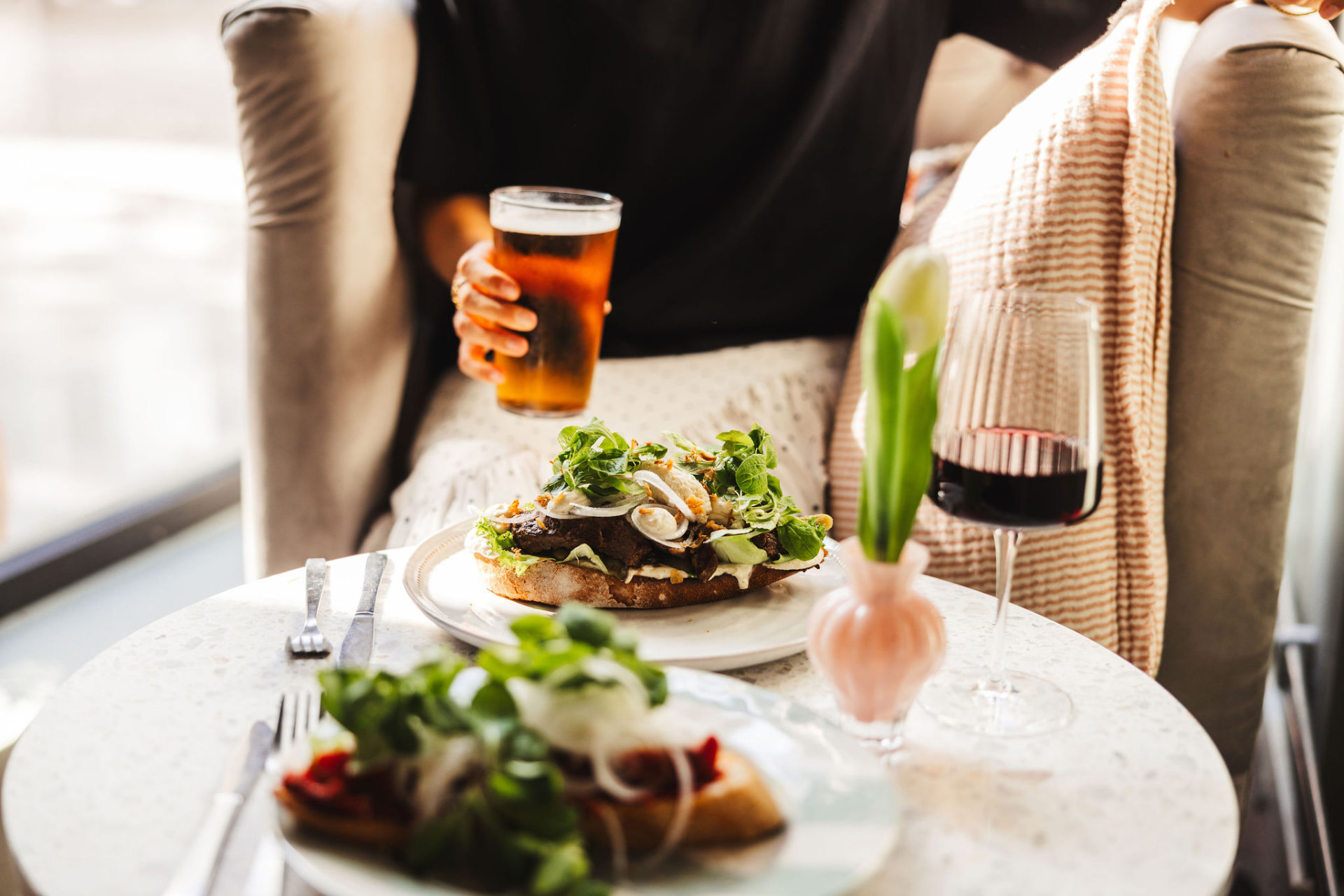 Makka med kött och sallad, öl och ett glas rödvin vid fönsterbordet